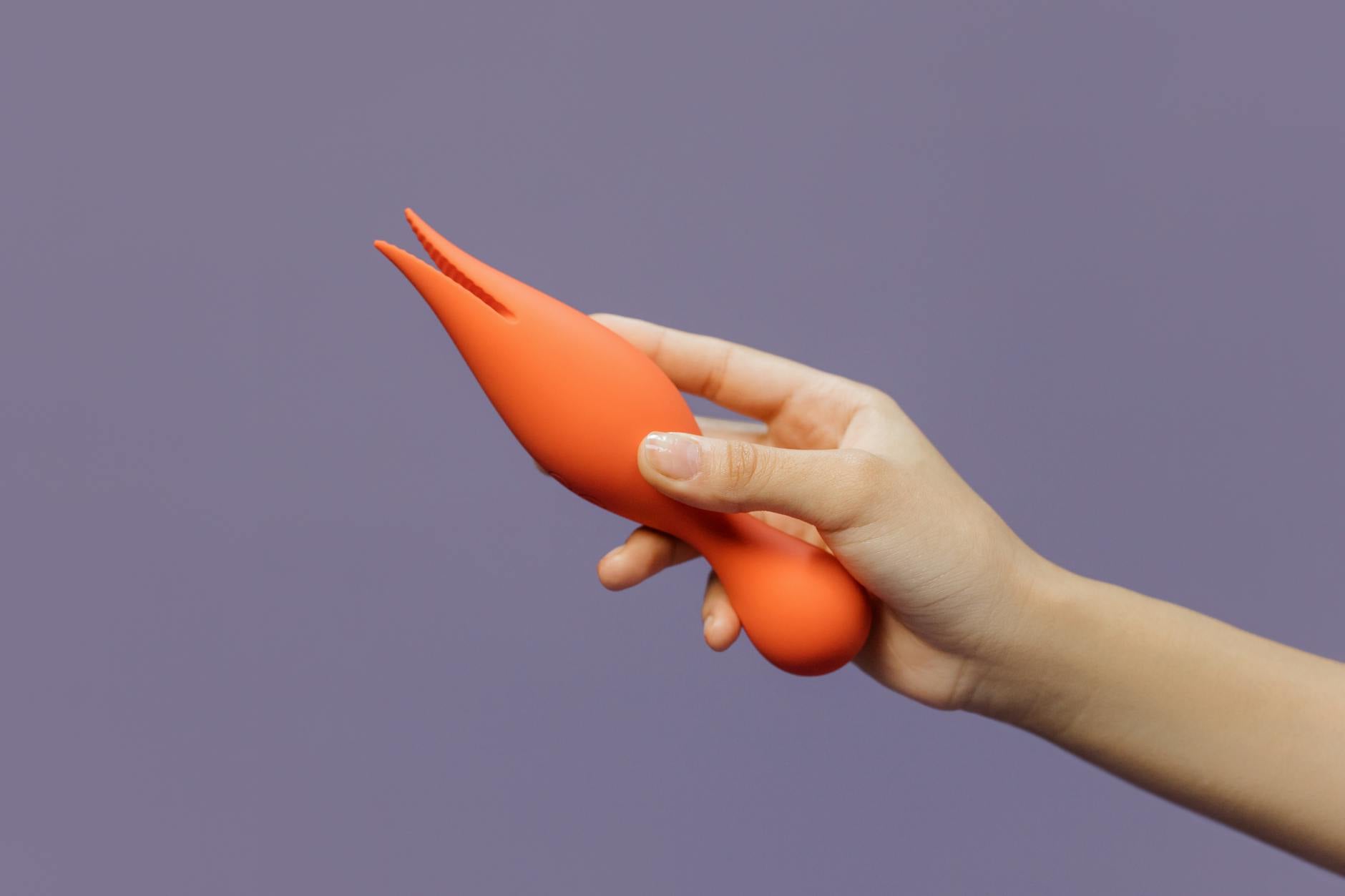 A close-up of a hand holding a vibrator against a minimalistic purple backdrop, showcasing modern sensuality and intimate touch between partners.