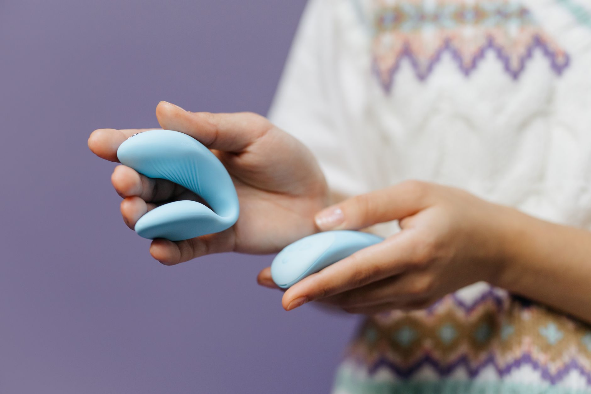 Hands holding a sleek blue vibrator together against a purple background, representing intimate partnership.
