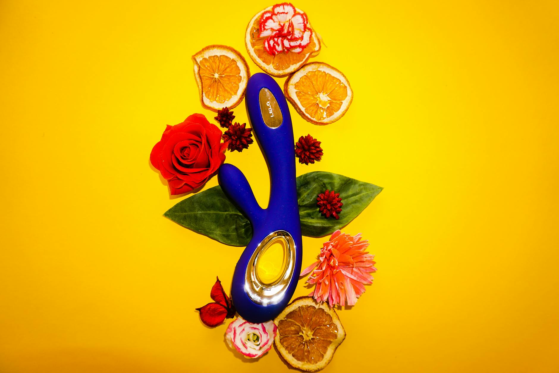 A blue lemon vibrator surrounded by fresh lemons and flowers on a bright yellow background
