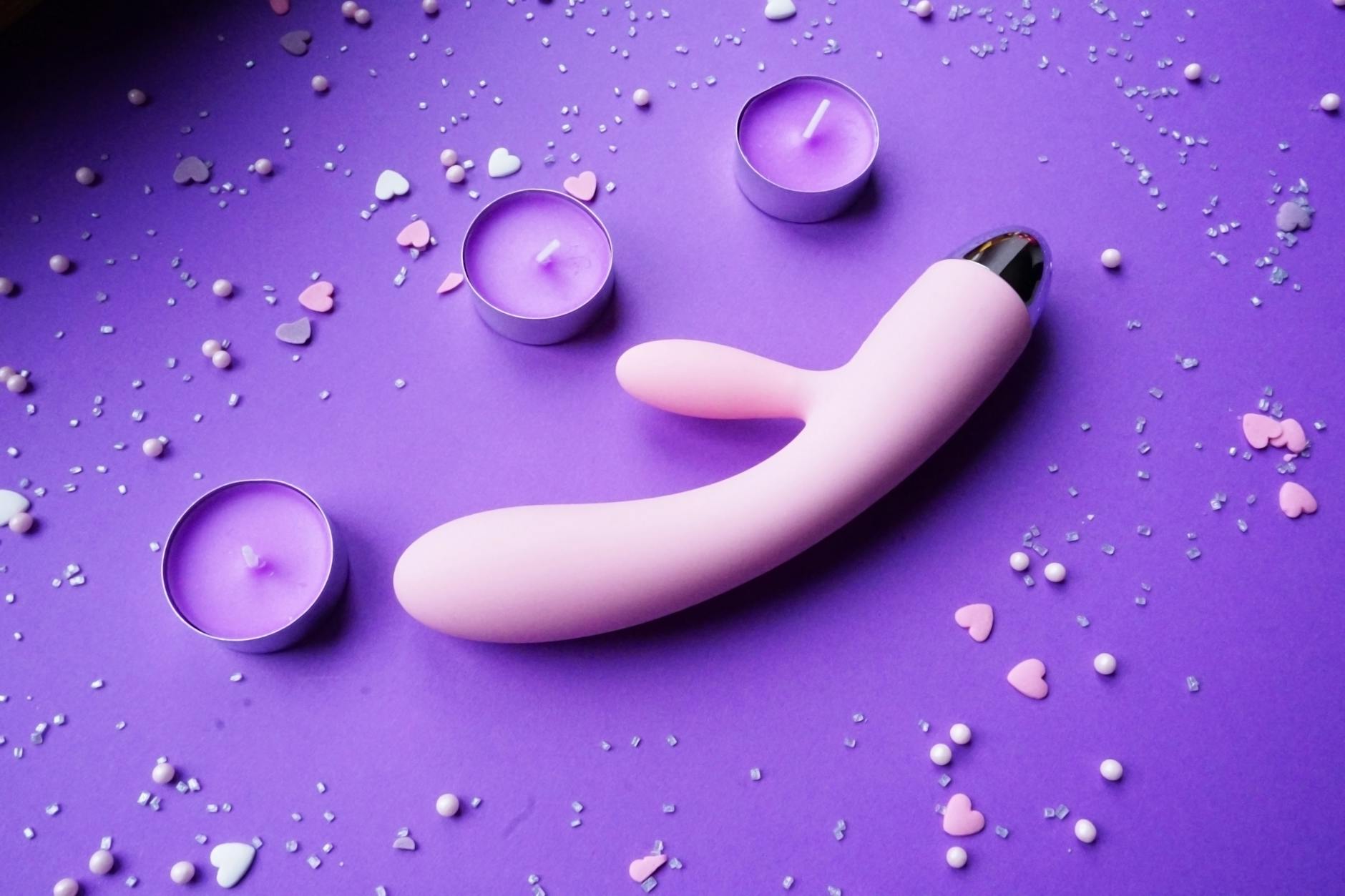 Pink vibrator on purple background with heart confetti and candles